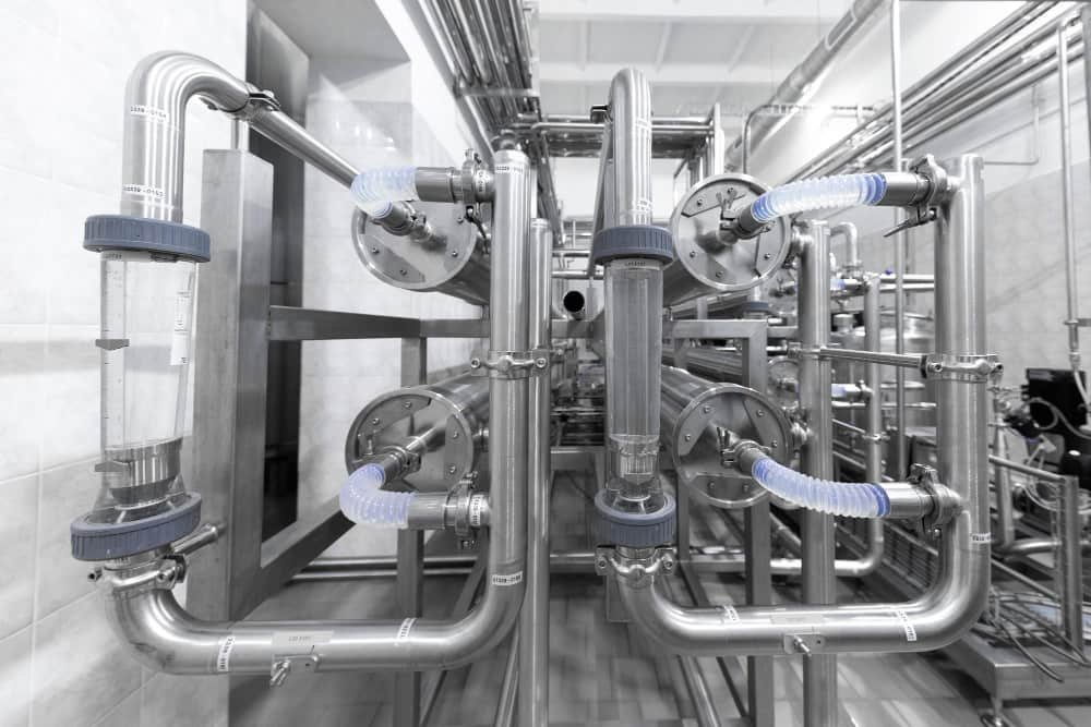 Installation moderne de réseaux de pompage industriel en acier inoxydable avec tuyauteries, filtres et débitmètres transparents dans une usine.