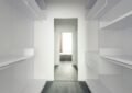 Corridor avec étagères blanches, sol gris, ouverture vers une pièce lumineuse avec lit
