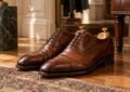 Paire de chaussures de ville marron posées sur un parquet avec des embauchoirs.