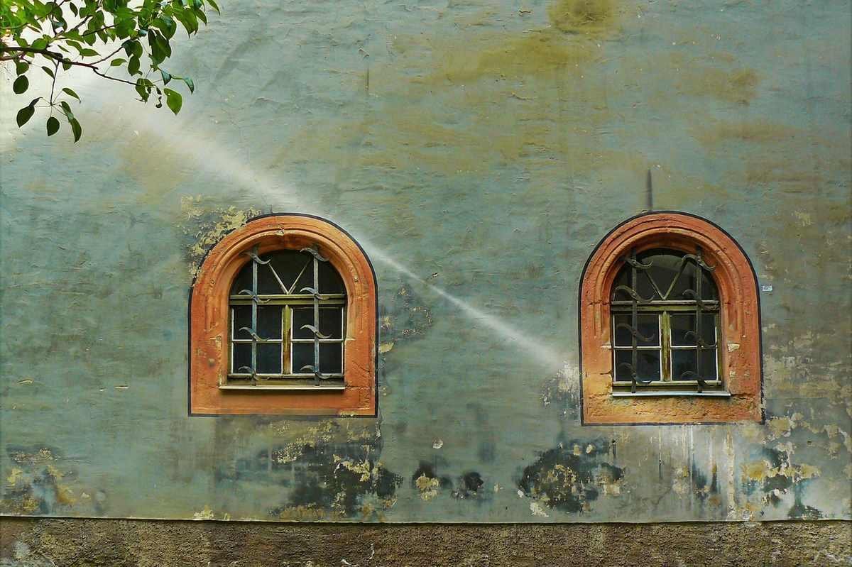 Façade verte patinée avec deux fenêtres en bois arquées, signes d'usure et de vieillissement