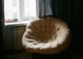 Fauteuil rond rembourré à côté d'une fenêtre avec radiateur et rideaux