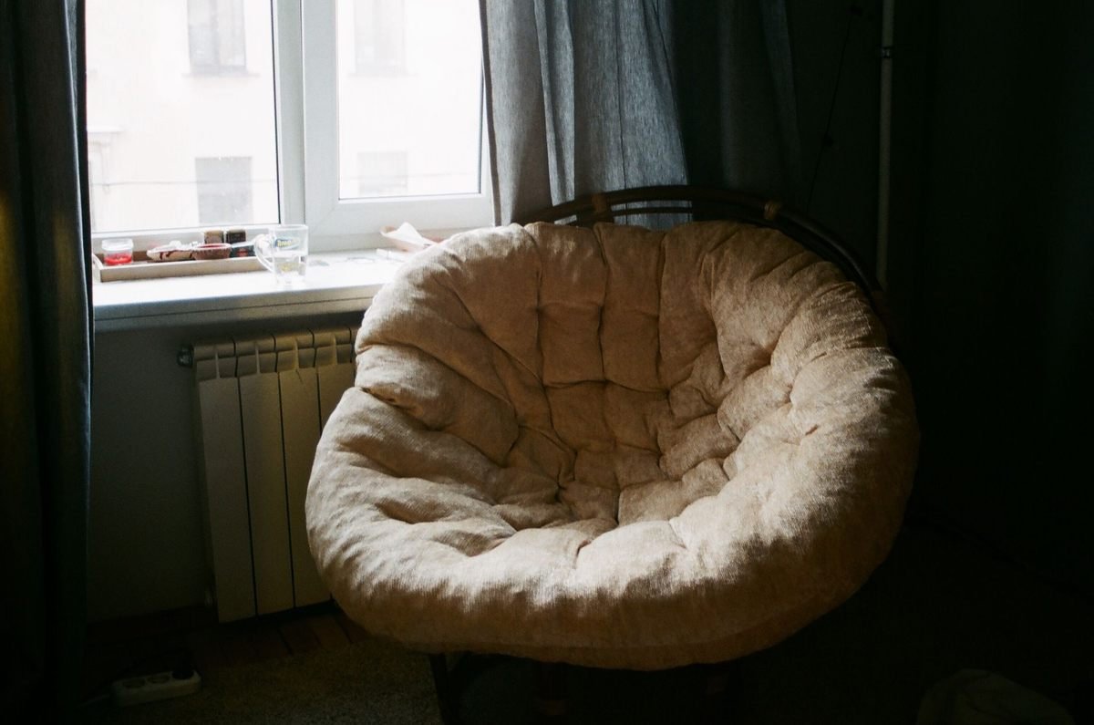 Fauteuil rond rembourré à côté d'une fenêtre avec radiateur et rideaux